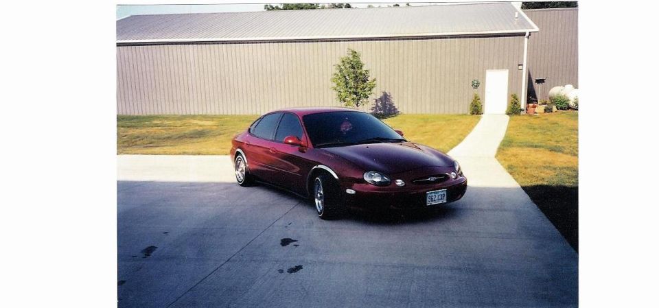 Maroon Ford Taurus front three-quarter on driveway beside tan metal building