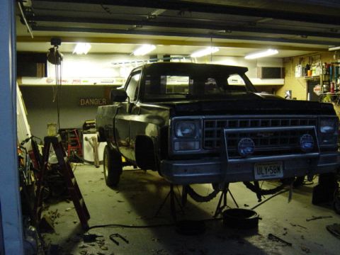 1987 Suzuki Samurai - Front view of a black pickup truck, possibly from the 1980s, undergoing maintenance in a garage.