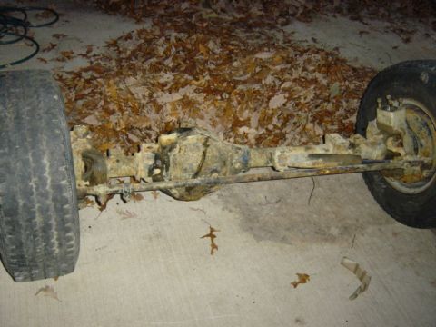 1987 Suzuki Samurai - A vehicle's rear axle assembly is shown, resting on a concrete surface amidst fallen leaves.