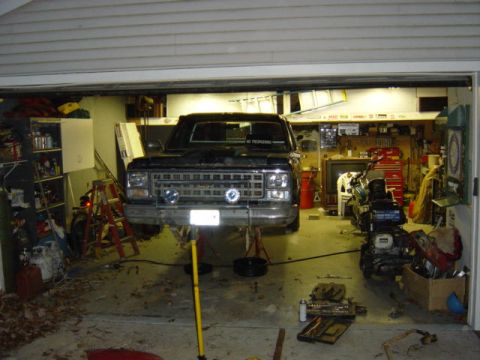 1987 Suzuki Samurai - A black pickup truck is raised on lifts inside a garage, with a motorcycle visible to the side.
