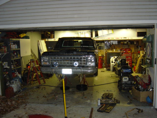Black pickup truck on lifts in a garage, front view. A motorcycle is parked to the right