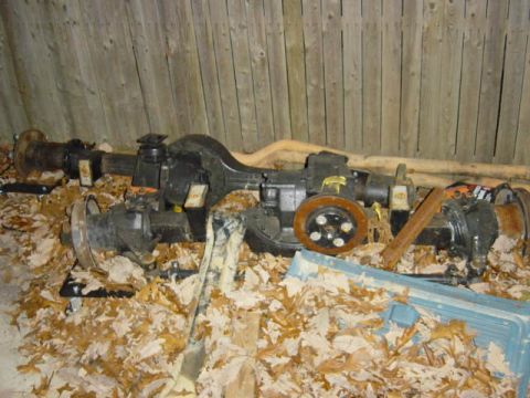 1987 Suzuki Samurai - Two axle assemblies are visible, one with a brake rotor, resting on a bed of fallen leaves.