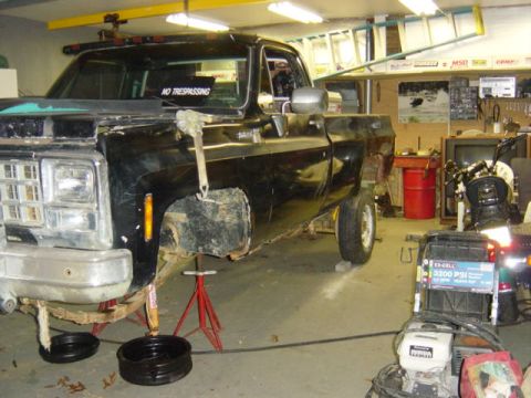 1987 Suzuki Samurai - Black pickup truck in a garage, lifted on jack stands with front end disassembled for work.
