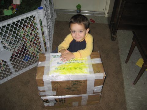 1981 Ford Bronco - A young child sits atop a large cardboard box, hands clasped, with shipping labels visible.
