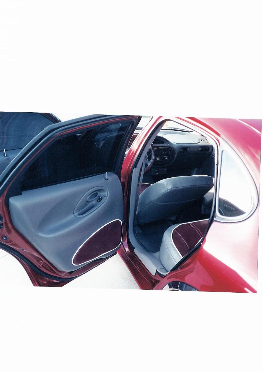 Open rear door of a red sedan showing custom gray and maroon interior with piped door panel and seats