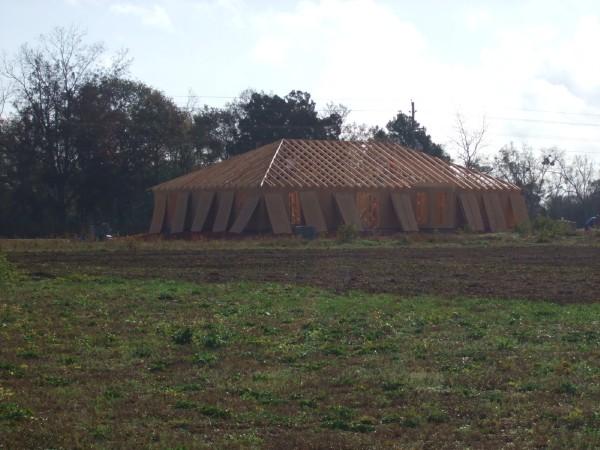 House framing and roof trusses visible in a field with trees in the background