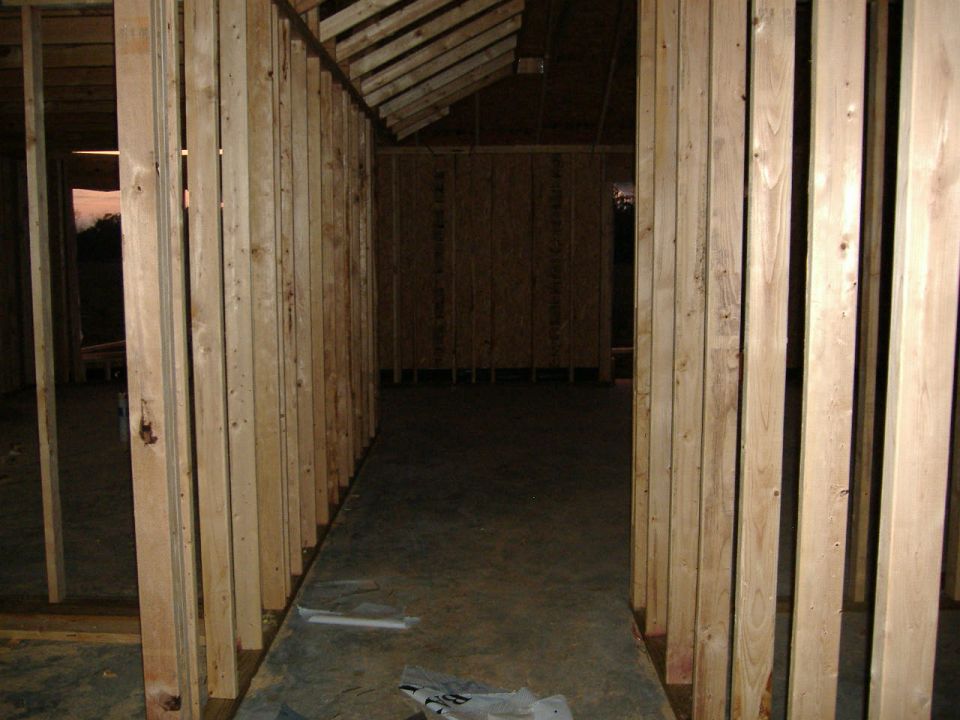 Interior view of a house under construction with exposed wooden studs and concrete floor