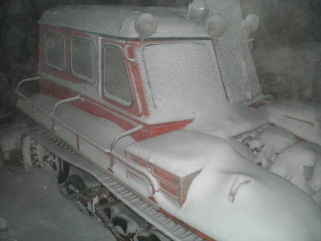 Red and white snow vehicle covered in snow, with tracks and multiple windows