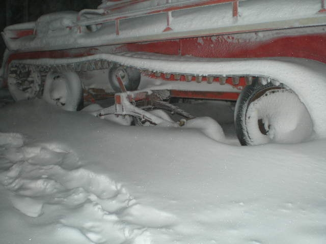 Red vehicle with tracks and wheels covered in snow, side view