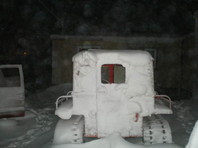 snow-covered tracked vehicle with red interior visible through window, another vehicle partially visible to the left