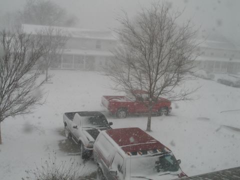 1995 Ford Bronco - Elevated view of a snow-covered parking area during heavy snowfall, with a red pickup, a dark pickup and a red full-size SUV wearing roof-m…