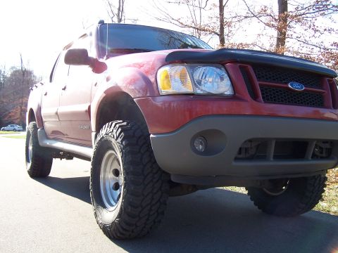 2002 Ford Sport Trac - A red 2002 Ford Sport Trac is parked outside with large off-road tires and a bug deflector.