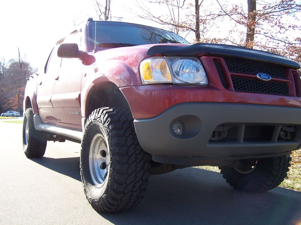 Red 2002 Ford Sport Trac with large off-road tires and a bug deflector on the hood