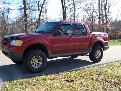 2002 Ford Sport Trac - A red Ford Explorer Sport Trac pickup truck is shown from a 3/4 front angle on a paved road with trees in the background.