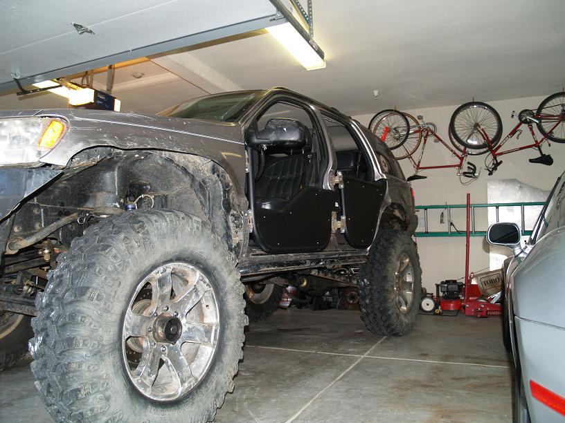 Modified 1999 Jeep Grand Cherokee with large off-road tires and removed doors in a garage