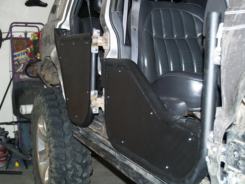 Interior of a Jeep showing custom black door panels and leather seats. A large off-road tire is visible