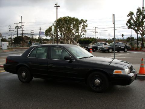 2005 Ford Crown Victoria - Side view of a black 2005 Ford Crown Victoria police car with other police vehicles behind it.