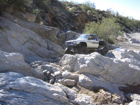 1987 Suzuki Samurai - A modified white pickup truck navigates a rocky, off-road terrain.