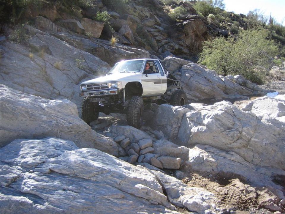 White 1984 Toyota pickup truck with oversized tires climbing rocky terrain