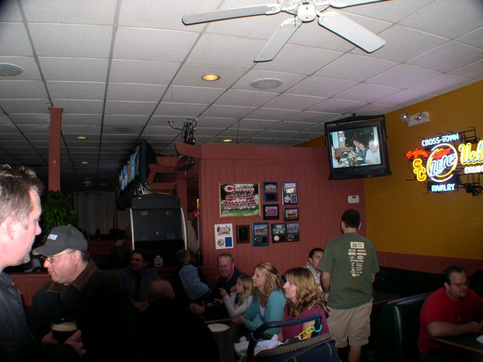 Interior of a bar with people sitting at tables and booths, TVs on the wall, and neon signs