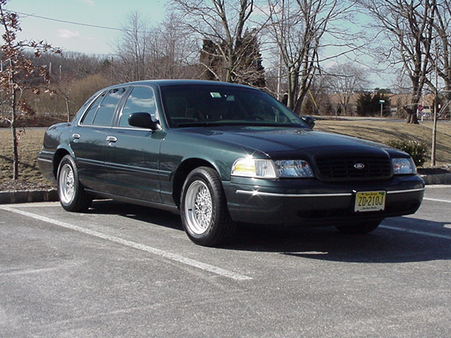 Dark green sedan parked in a lot, front 3/4 view. Chrome wheels, black grille, license plate 20-210J
