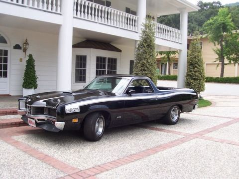 1972 Ford Ranchero - This black pickup truck with racing stripes is parked in front of a large white house.
