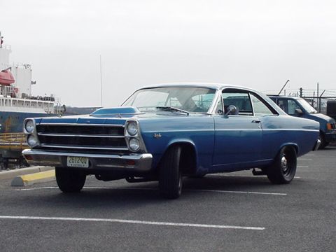 1966 Ford Fairlane - A blue 1966 Ford Fairlane coupe is parked in a lot, with a ship visible in the background.