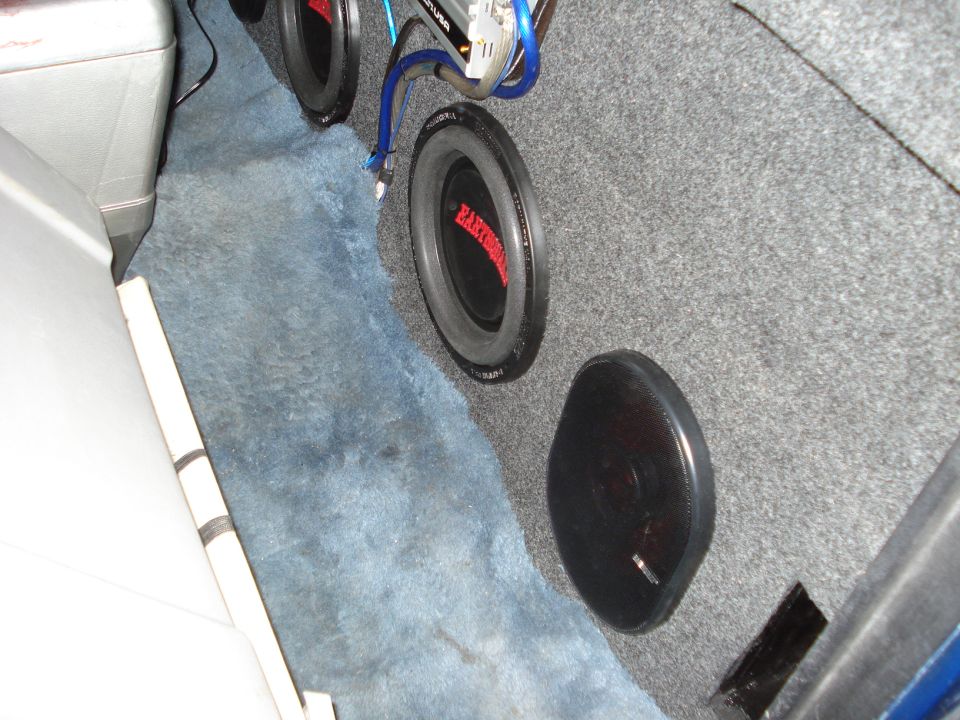 Car interior with three subwoofers and amplifier, gray carpet lining, blue floor matting