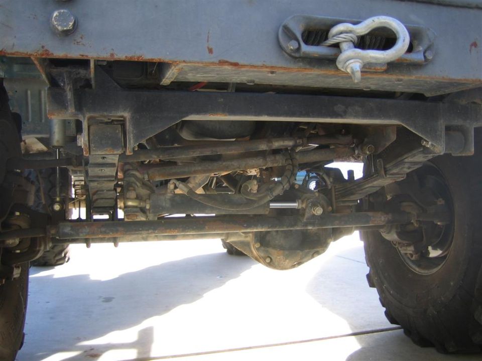 Undercarriage of a vehicle with leaf springs, differential, and steering components visible. A winch hook is mounted on the frame
