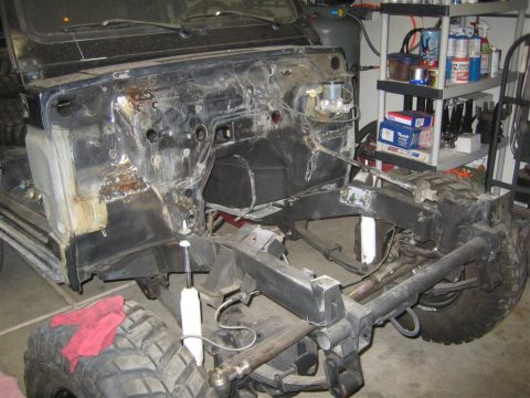 1987 Suzuki Samurai - Front view of a Suzuki Samurai mid-teardown in a home garage: engine and front sheet metal removed, showing the rusty, patched firewall, em…