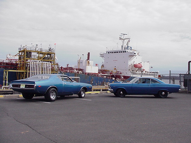 Two blue classic cars, a 1971 Dodge Charger and a 1966 Ford Fairlane, parked by a ship