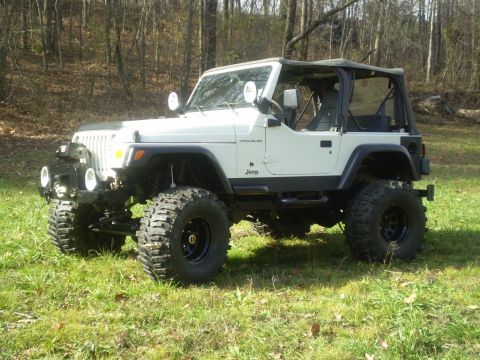 1997 Jeep Wrangler - A white Jeep Wrangler with a soft top is parked in a wooded area.