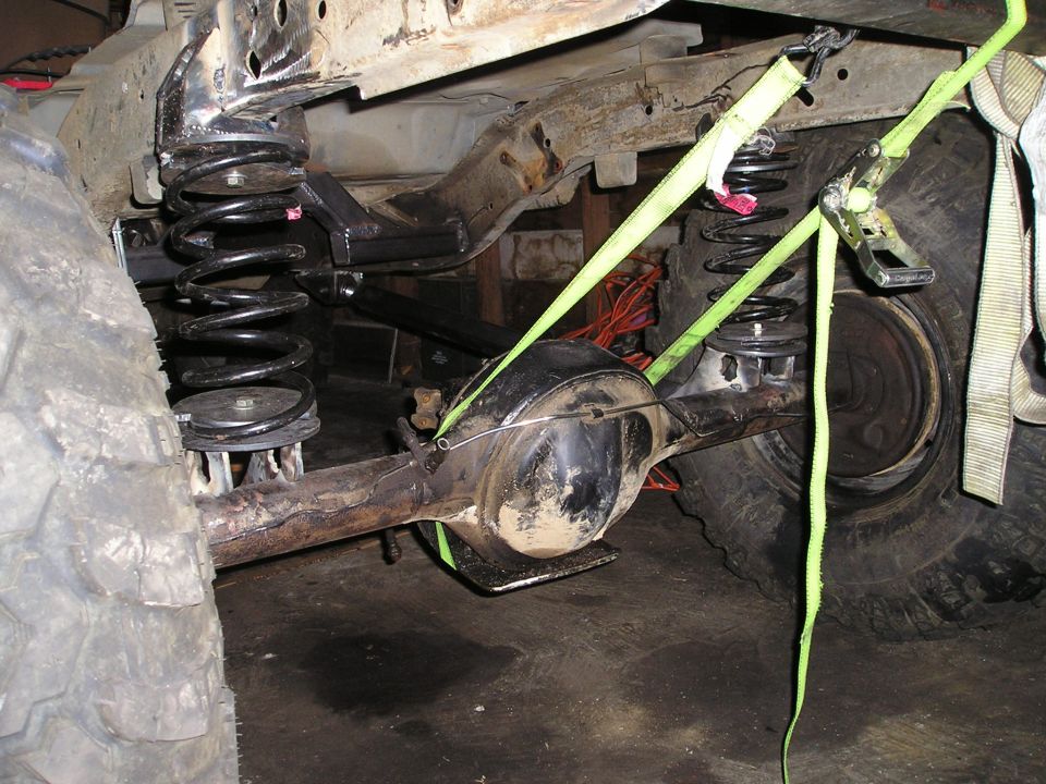 close-up of rear axle and suspension springs on a vehicle being worked on, held by straps