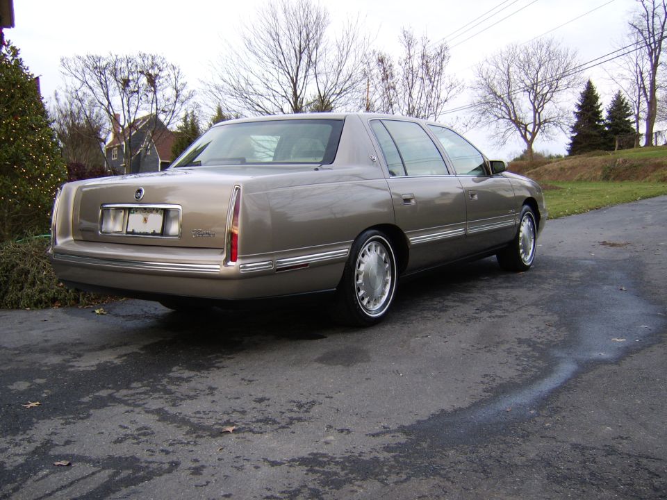 Gold Cadillac DeVille sedan, rear three-quarter view on wet driveway