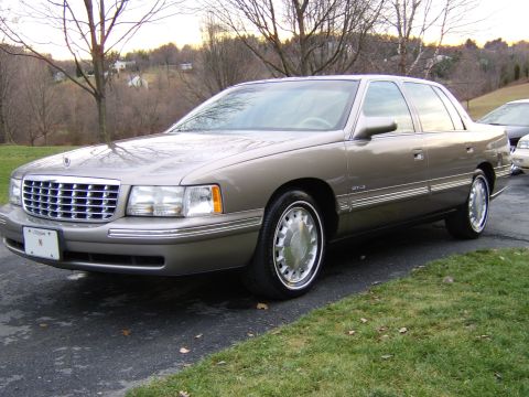 1996 Mercury Grand Marquis - A tan Cadillac sedan is parked on an asphalt driveway with a grassy area to the side.