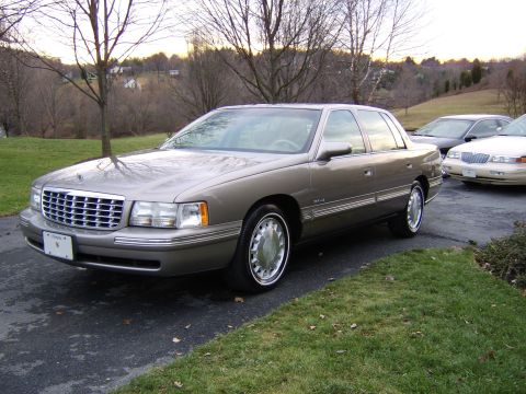 1996 Mercury Grand Marquis - A tan Cadillac DeVille is parked in front of another car on a driveway.