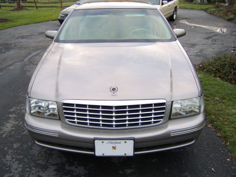1996 Mercury Grand Marquis - A tan Cadillac sedan is parked on a driveway, with another vehicle visible in the background.