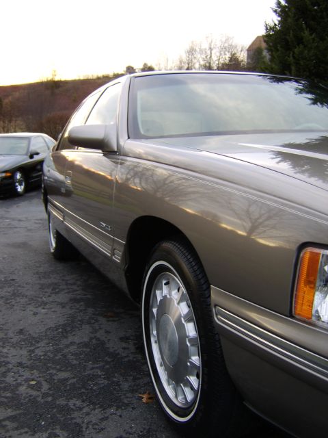 1996 Mercury Grand Marquis - A tan Cadillac DeVille is parked on an asphalt surface, with another car visible in the background.