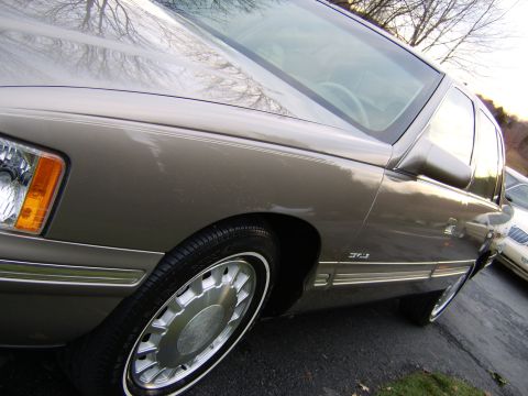 1996 Mercury Grand Marquis - A tan sedan with chrome accents and a distinctive wire wheel cover is parked on an asphalt surface.
