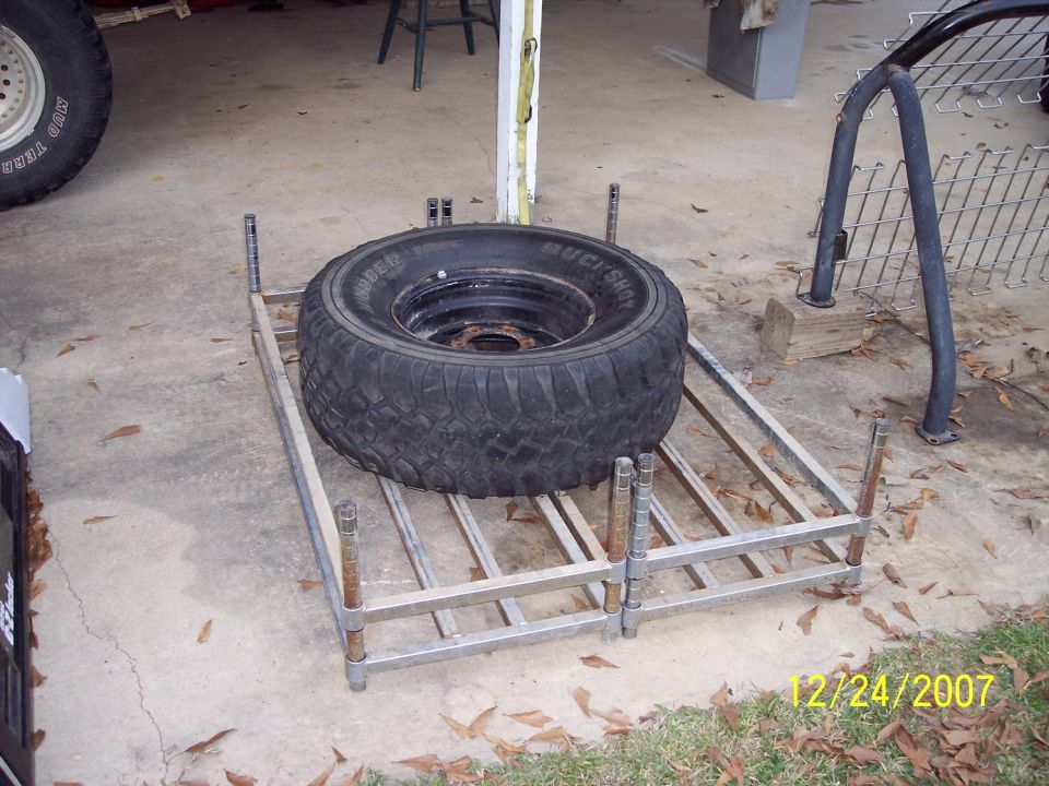 Spare tire on a metal rack, with a portion of a vehicle tire visible on the left