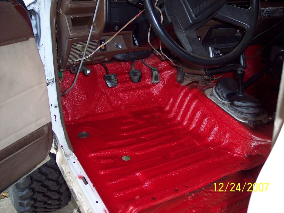 Interior floor of a vehicle with red spray-on bedliner, showing pedals and gear shifter