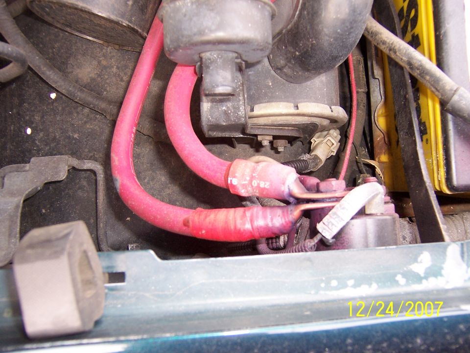 Red battery cables attached to a fender-mounted starter solenoid in an engine bay