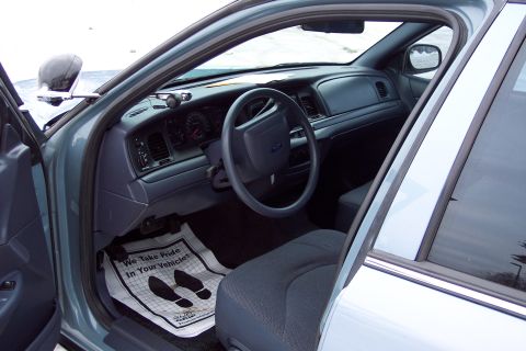 2001 Ford Crown Victoria - The interior of a Ford Crown Victoria, the driver's side dashboard and seat, with a floor mat that reads 'We Take Pride In Your Vehicle.'