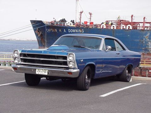 1966 Ford Fairlane - A blue coupe with a prominent hood scoop is parked near a large cargo ship named 'CAPTAIN H. A. DOWNING'.