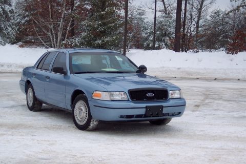 2001 Ford Crown Victoria - This blue 2001 Ford Crown Victoria sedan is parked on a snowy surface with trees in the background.