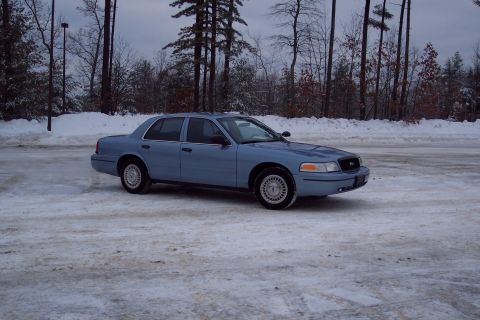 2001 Ford Crown Victoria - Blue 2001 Ford Crown Victoria sits on a snow-covered asphalt lot with trees in the background.