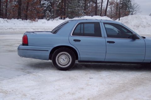 2001 Ford Crown Victoria - A light blue 2001 Ford Crown Victoria sedan is parked on a snowy surface with trees and snowbanks in the background.