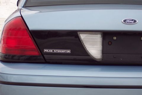 2001 Ford Crown Victoria - The rear of a light blue 2001 Ford Crown Victoria Police Interceptor, showing the Ford badge and 'Police Interceptor' emblem.