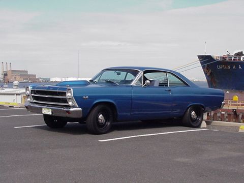 1966 Ford Fairlane - A blue 1966 Ford Fairlane coupe is parked in a lot, with a large ship visible behind it.
