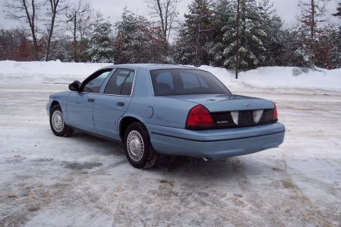2001 Ford Crown Victoria - A light blue sedan sits on a snow-covered lot with trees in the background.
